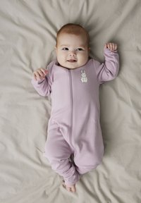 Svijetloroza beba bodi s dugim rukavima i prednjim zatvaračem, s malim bijelim dizajnom zeca na prsima, odložen na bež pozadini.