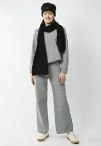 Grijs gebreid sweater- en broekset, gecombineerd met een zwarte ribbelbeanie en bijpassende sjaal. Witte sneakers met beige accenten maken de look compleet.