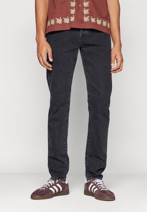 Person wearing faded black jeans, maroon Adidas sneakers with white stripes, and a maroon shirt with white floral embroidery.