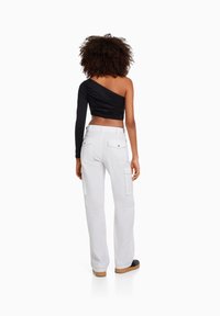 Svart enaxlad crop top i kombination med vita cargobyxor med fickor. Outfiten har en texturerad tyg och en figurnära design.