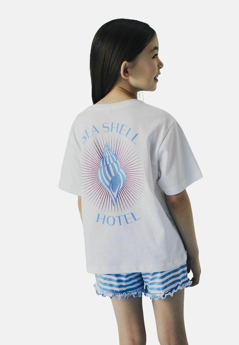Witte katoenen t-shirt met een blauwe schelpgrafiek en de tekst "SEA SHELL HOTEL", gecombineerd met blauw-wit gestreepte rucheshort.