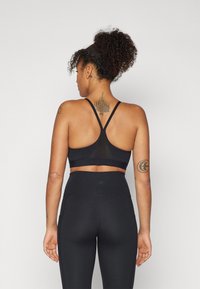 Sostén deportivo negro con diseño de espalda nadadora, que presenta un panel de malla. Combinado con leggings negros de cintura alta, estilizados con una textura suave.