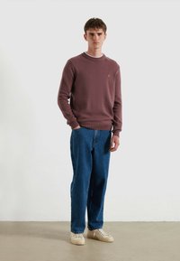 Maglione viola testurizzato con polsini a coste, abbinato a jeans blu a gamba dritta e sneaker beige. Design semplice e vestibilità classica.