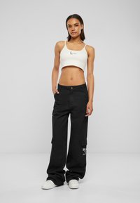 Débardeur blanc coupé avec un logo noir, associé à un pantalon cargo noir ample avec des poches latérales et un imprimé logo. Baskets blanches.