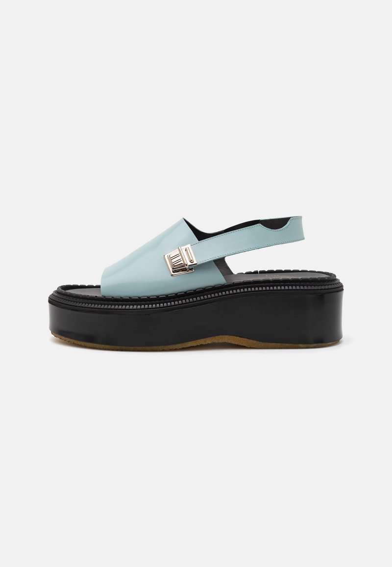 Sandaler med åben hæl i lyseblå, blank overdel og en tyk sort platform sål. Har en dekorativ metallisk spænde og kontrasterende teksturer.