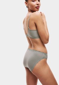 Světle zelený bavlněný set spodního prádla s krajkovým lemováním kolem pasu a ramínek podprsenky, který se vyznačuje bezešvým designem a hladkou texturou.