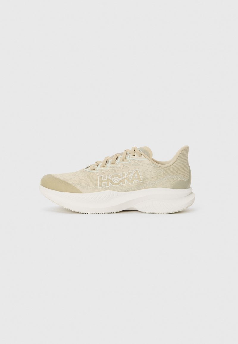 Chaussure de sport beige clair avec un dessus texturé, un bout rond et une semelle épaisse et rembourrée. Présente un logo blanc bien visible sur le côté.