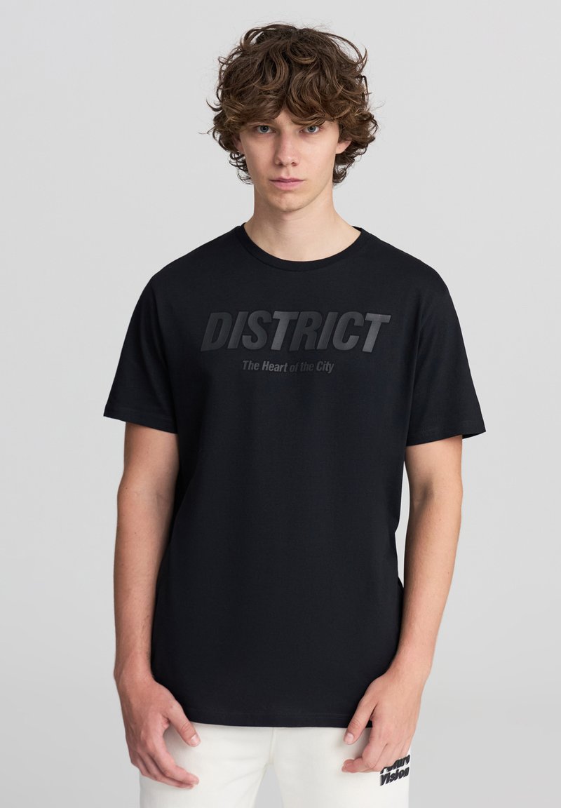 Maglietta nera in cotone con collo rotondo, caratterizzata da una stampa audace e testurizzata "DISTRICT" e "Il Cuore della Città" in un font più leggero.