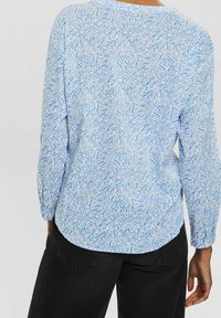 Langarmhemd mit einem hellblauen und weißen abstrakten Muster, aus weichem Stoff. Gerundeter Saum und lockere Passform, kombiniert mit dunklen Hosen.