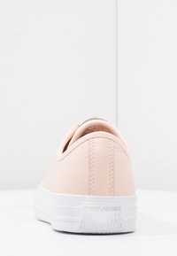 Baskets roses texturées avec une finition lisse, semelle en caoutchouc blanche, et logo embossé "Converse ALL STAR" sur le talon. Vue de dos.