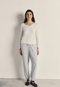 White long-sleeve V-neck shirt made of soft fabric, paired with light gray textured sweatpants and black sandals, standing against a plain background.