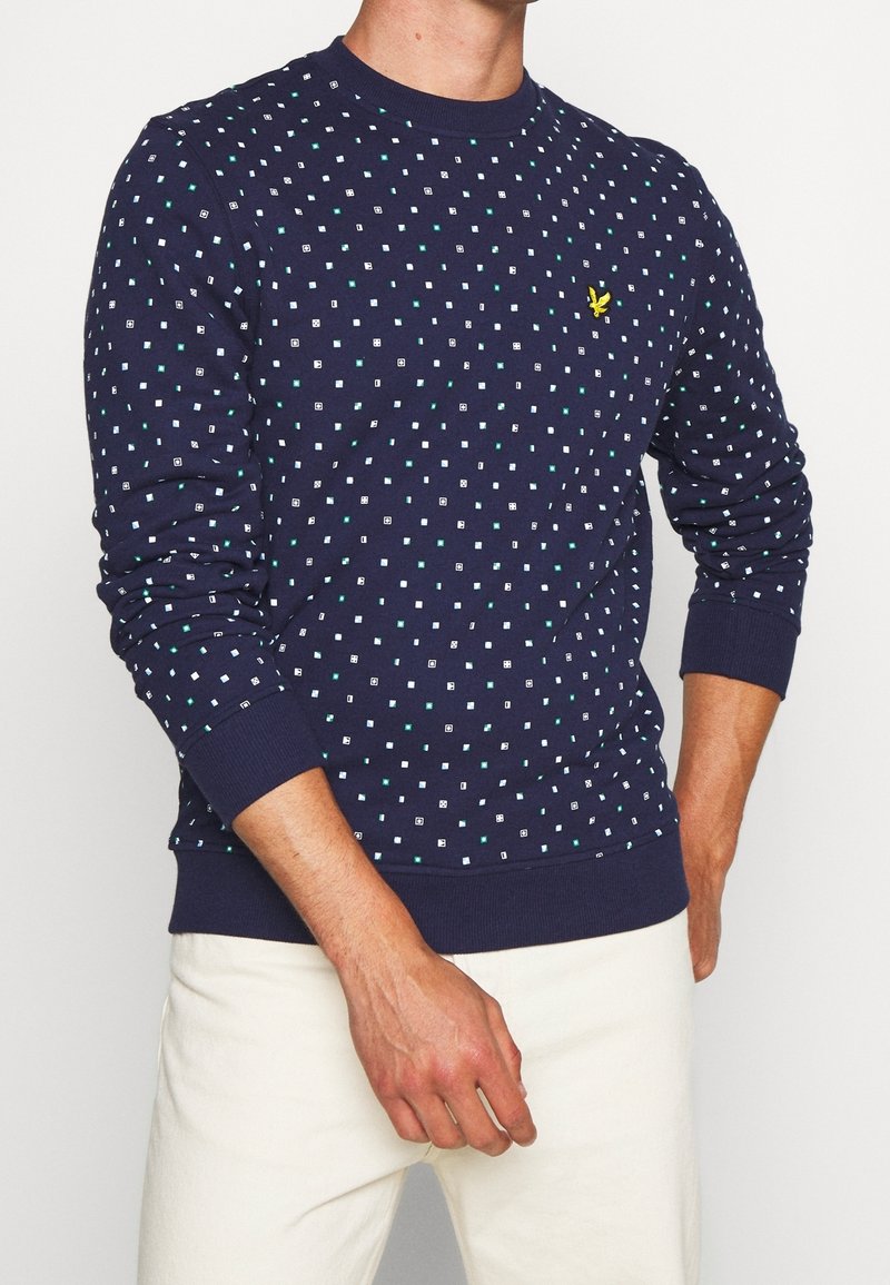 Felpa blu navy con motivo a pois composto da quadrati bianchi e turchesi, maniche a costine e un piccolo logo giallo sul petto.