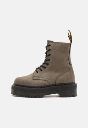 Graue Leder-Stiefelette mit schwarzer Gummi-Plattformsohle, runder Zehenpartie und schwarzen Schnürsenkeln. Mit einem gelben Zugband an der Rückseite.