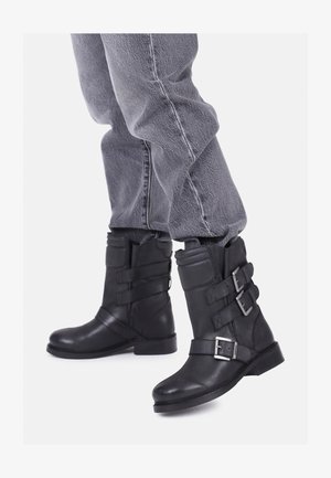 Črne usnjene gležnjarje z več trakovi in srebrnimi zaponkami. Okrogla ponta in ravna podplat. Nosi se jih z ohlapnimi sivimi kavbojkami.