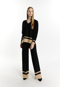 Maglione nero a maglia con scollo a V e maniche lunghe, orlo a righe beige e nere. Pantaloni neri a gamba larga con accenti a righe beige alle caviglie.