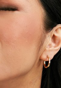 Goldene Creole, die am Ohr getragen wird, mit einer polierten, glatten Oberfläche, runder Form und ohne Verzierungen oder Muster.