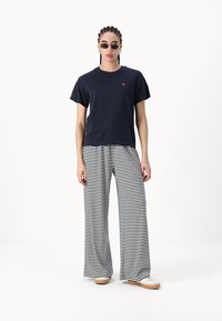 T-shirt en coton bleu marine à manches courtes avec un petit logo en forme de cœur rose, associé à un pantalon large rayé noir et blanc.