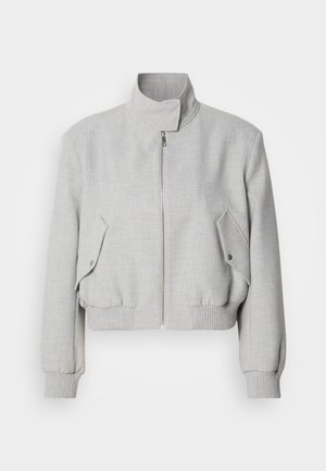 Világosszürke, rövid fazonú dzseki magas gallérral, cipzáras záródással és bordázott mandzsettával. Két ferde oldalzsebével rendelkezik, amelyek patentgombbal záródnak.