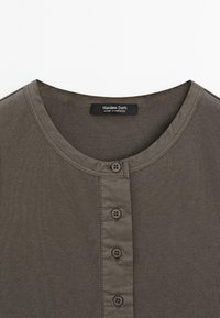 Khaki henley košile s kulatým výstřihem, čtyřtlačítkovým zapínáním a vroubkovanou texturou. Štítek říká "Massimo Dutti", vyrobeno v Maroku.
