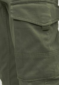 Pantalons cargo vert olive, avec une poche latérale, des coutures décoratives et un tissu doux et texturé avec une finition durable.