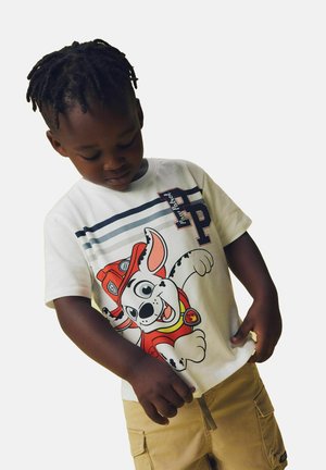 Weißes T-Shirt mit einem bunten Cartoon-Hund in Feuerwehruniform, ergänzt durch marineblaue horizontale Streifen und Logos auf der Brust.