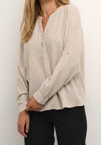 Chemise à rayures beige et blanche à manches longues avec col, patte de boutonnage et manches à poignets, fabriquée en tissu léger.