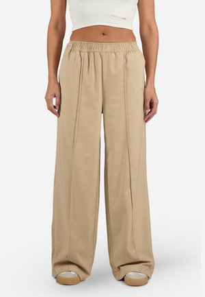 Široké béžové kalhoty s elastickým pasem, hladkou texturou a dvěma předními sklady. Stylizované s cropped topem a ležérní obuví.