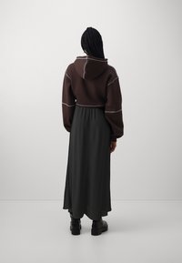 Barna, cropped kapucnis pulóver szürke varrással, hosszú fekete szoknyával párosítva. A modellen fekete, vastag sarkú csizmák vannak. Egyszerű, modern dizájn.