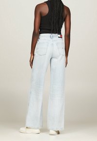 Jeans de pierna ancha de color azul claro con una cintura alta, que presentan un cierre de botón, dos bolsillos traseros y un parche con el logo en la cinturilla.