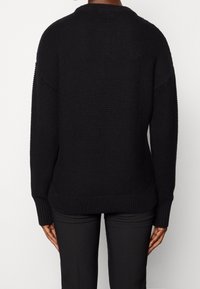 Musta neulepaita pyöreällä pääntiellä ja ribbauskoristeilla hihoissa ja helmassa. Ominaisuuksina rento malli ja teksturoitu pinta.