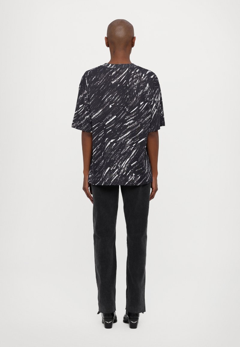 Sort og hvid mønstret kortærmet skjorte, afslappet pasform, båret sammen med sorte lige bukser og sorte stiletter, set fra ryggen.