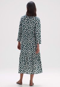 Lång klänning med ett geometriskt mönster i teal och kräm, flared lagerkjol, trekvartslånga ärmar och mjukt, lättviktigt tyg.