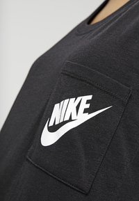 Černé bavlněné triko s kulatým výstřihem a přední kapsou. Na kapse je bílý logo Nike. Hladká textura.