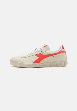 Sneaker in pelle beige con una striscia diagonale rossa brillante, lacci bianchi e suola testurizzata. Logo visibile sul lato e sulla linguetta.