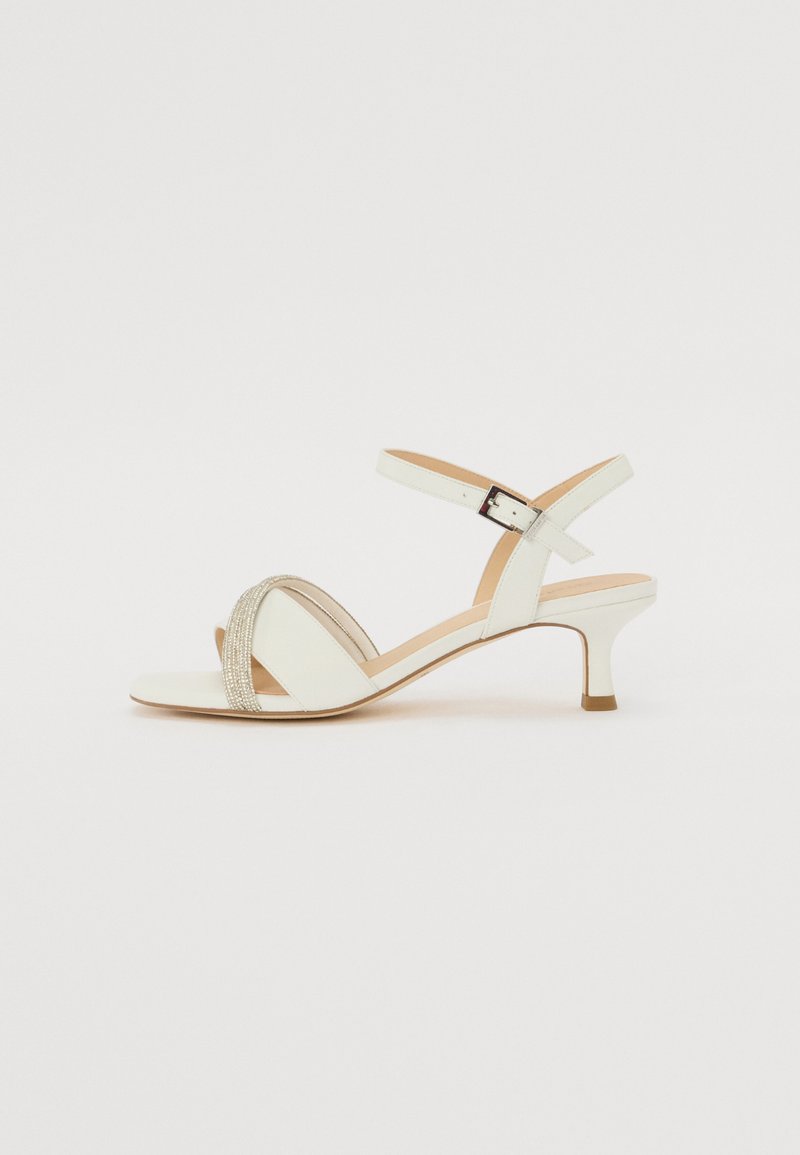 Valged kontsad, millel on madal plokknina, risttraksiga disain, kaunistatud metalliliste detailidega. Sile nahast tekstuur.