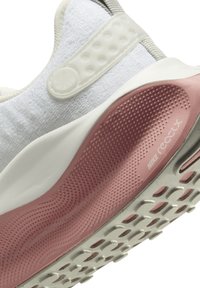 Les chaussures Nike React présentent un dessus texturé blanc, une semelle rose avec des rainures flexibles et un talon en caoutchouc proéminent pour un bon amorti.