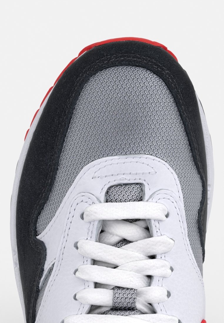Baskets de sport avec une tige en maille grise, des accents en suède noir, des lacets blancs et des détails rouges au niveau du talon. Surfaces texturées et design en couches.