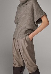 Vaaleanharmaa neulepusero, jossa korkea resorikaulus ja käännetyt hihat, yhdistettynä väljäsäärisiin taupenvärisiin housuihin, joissa on kalvosimet lahkeissa.