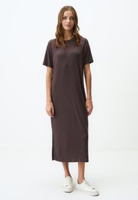 Robe midi marron à manches courtes, en texture côtelée, avec un col rond et des fentes sur les côtés, associée à des baskets blanches. Design minimaliste.