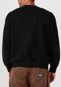 Maglione nero a maglia con maniche a costine e colletto rotondo, dalla vestibilità comoda e texture liscia, abbinato a pantaloni in corduroy marroni.