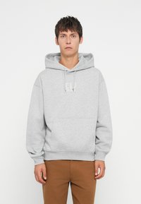Sudadera gris con un bolsillo frontal, capucha con cordón y logo de GAP en blanco. Combinada con pantalones marrones, con puños y dobladillo acanalados.