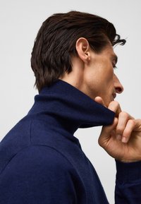 Marineblauer Rollkragenpullover mit weicher Textur und lockerer Passform. Der Kragen ist nach unten gefaltet und zeigt das glatte Strickmuster.