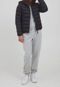 Veste rembourrée marine avec une capuche, fermeture éclair à l'avant et poignets élastiques, associée à un pantalon de survêtement gris et des baskets blanches pour un look décontracté.