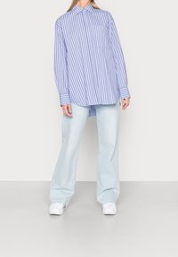 Stripet langærmet skjorte i lyseblå og hvid med en knappet krave, der har en enkelt brystlomme og brede manchetter. Sammen med lyse jeans.