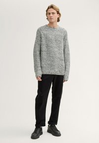 Suéter de punto gris con textura, de mangas largas y cuello redondo, combinado con pantalones negros acanalados y zapatos negros con cordones.