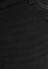 Gros plan sur un tissu en denim noir avec une déchirure effilochée près du coin supérieur droit et des coutures visibles à la ceinture.