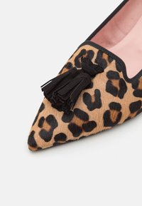 Chaussure plate à bout pointu imprimé léopard avec détail pompon noir et bordure noire sur fond clair.