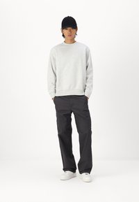 Felpa grigia a collo rotondo, abbinata a pantaloni cargo neri con tasche laterali. Indossata con sneakers bianche e un cappellino nero.