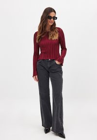 Burgundy plisseret langærmet top med en tætsiddende talje, parret med højtaljede sorte brede jeans og spidse sorte pumps.