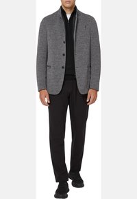 Gray textured blazer with black buttons, two front pockets, and a collar, layered over a black zip-up sweater and paired with black pants and shoes.